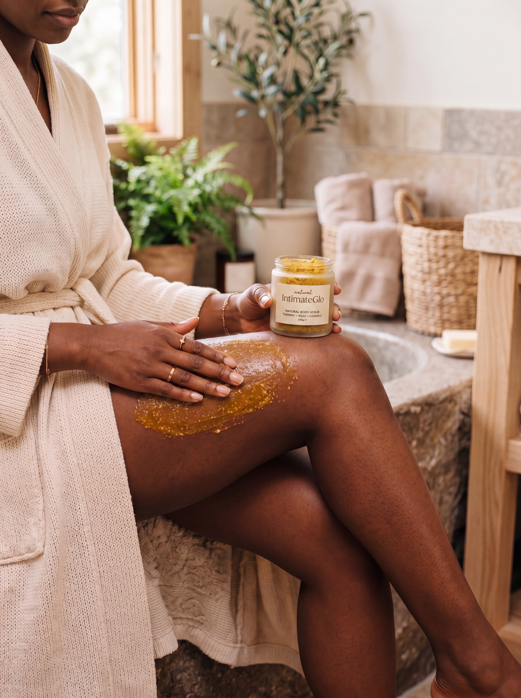 Woman applying IntimateGlo golden body scrub to skin in spa bathroom